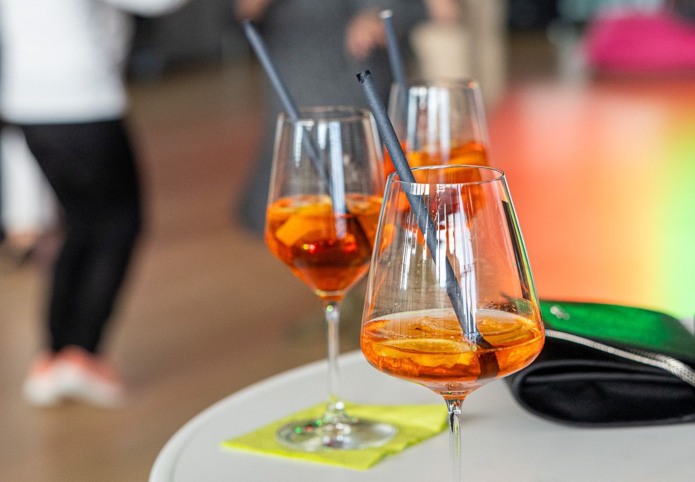 Drei Weingläser gefüllt mit orangefarbener Flüssigkeit auf einem weißen Stehtisch
