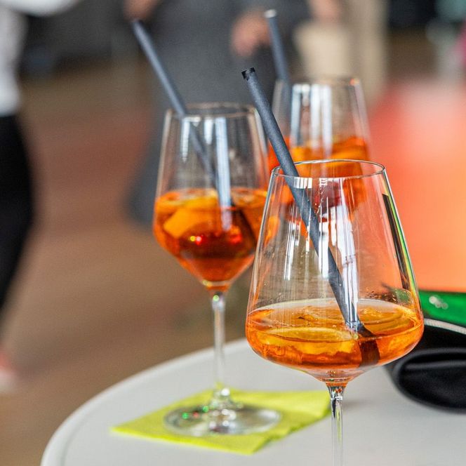 Drei Weingläser gefüllt mit orangefarbener Flüssigkeit auf einem weißen Stehtisch