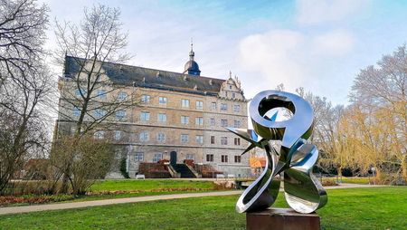 Ein silbernes Kunstobjekt auf einer Wiese, im Hintergrund das Schloss Wolfsburg